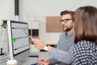 Zwei Presonen schauen auf einen Bildschirm, auf dem das Dashboard der Lösung Detailed Projectmanagement zu sehen ist