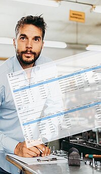 A man reviews an inspection plan on a digital device while working in a workshop filled with tools and equipment.